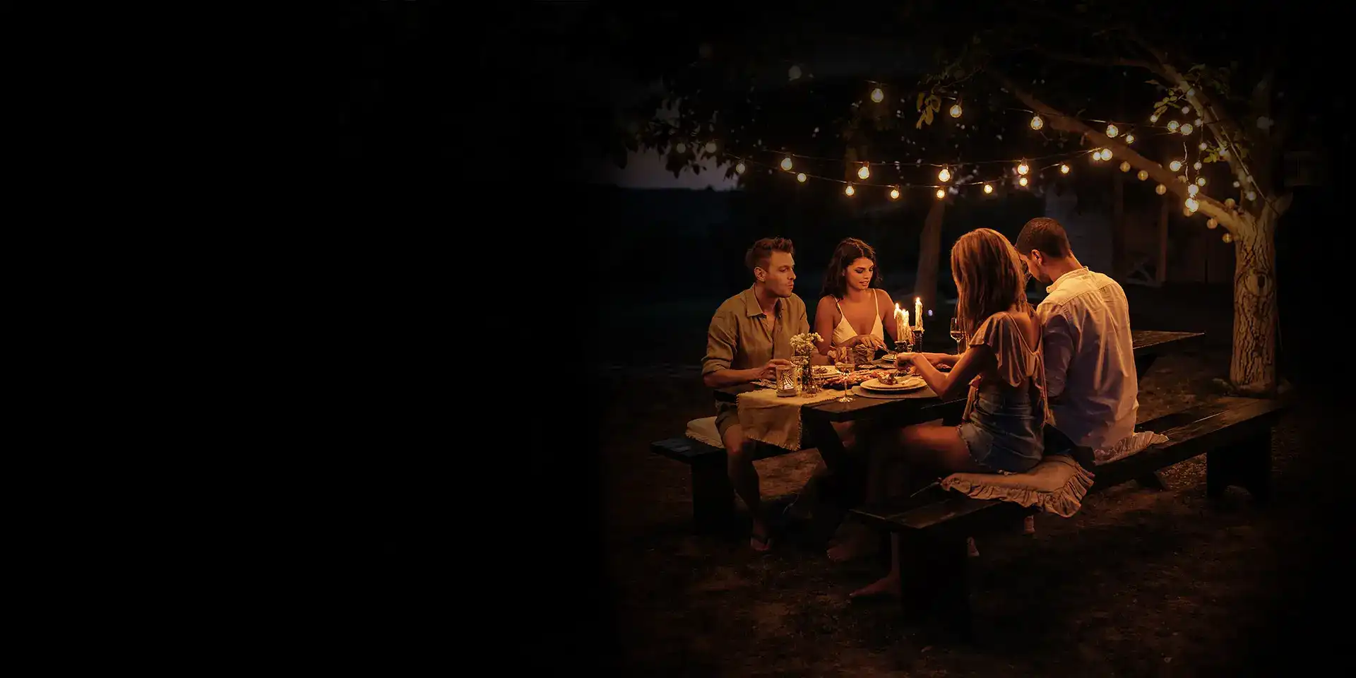 Zwei Pärchen genießen ein Candle-Light-Dinner neben einem Wohnmobil